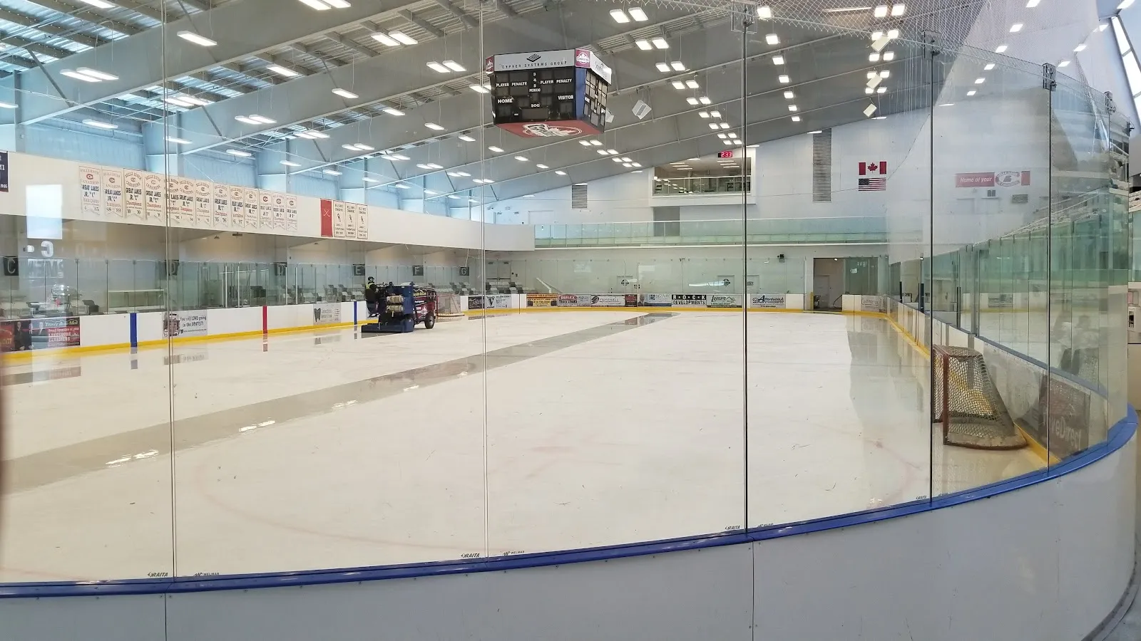 Una pista de hielo vacía vista a través del cristal desde un extremo, con la pulidora de hielo junto a las vallas del fondo, el marcador arriba y estandartes en la pared del fondo. — Atlas Tube Recreation Centre