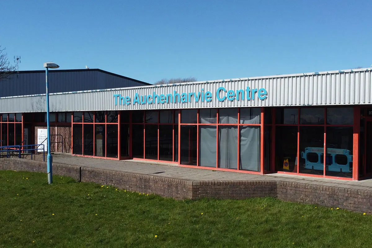 The single-storey front of the Auchenharvie Centre, with its teal name sign above red-framed windows. — Auchenharvie Ice Rink