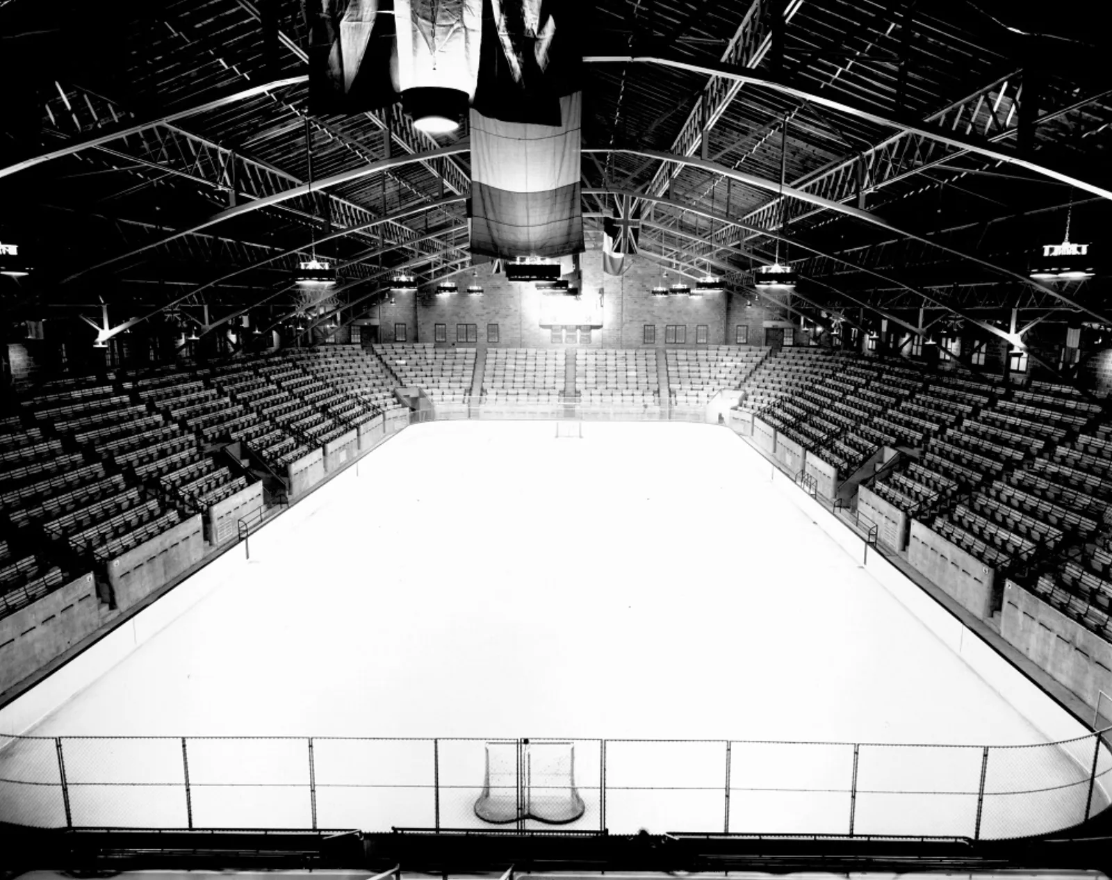 A 1939 archival photo looking down the length of the full ice sheet inside the Auditorium de Verdun, with empty wooden bleachers, a hockey net and the building's arched steel roof trusses. — Auditorium de Verdun