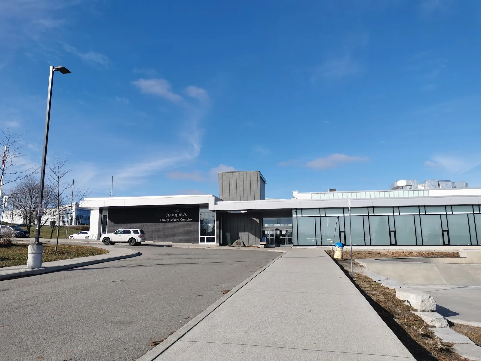 The white-and-glass front of the Aurora Family Leisure Complex seen from the paved approach under a blue sky. — Aurora Family Leisure Complex