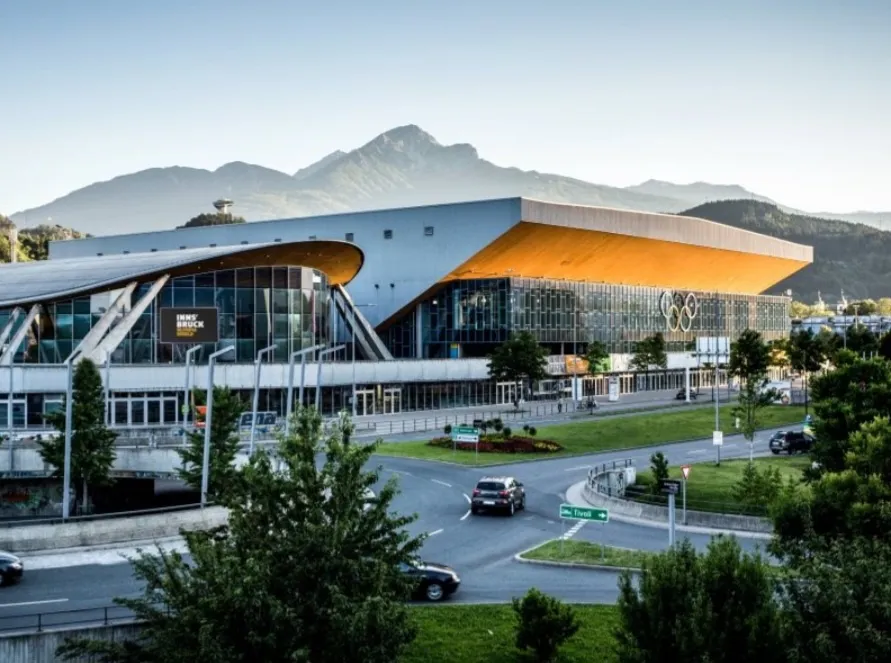 The Olympiaworld Innsbruck with its sweeping roof seen across the roundabout, with the mountains behind. — Olympiaworld Außeneisring Innsbruck