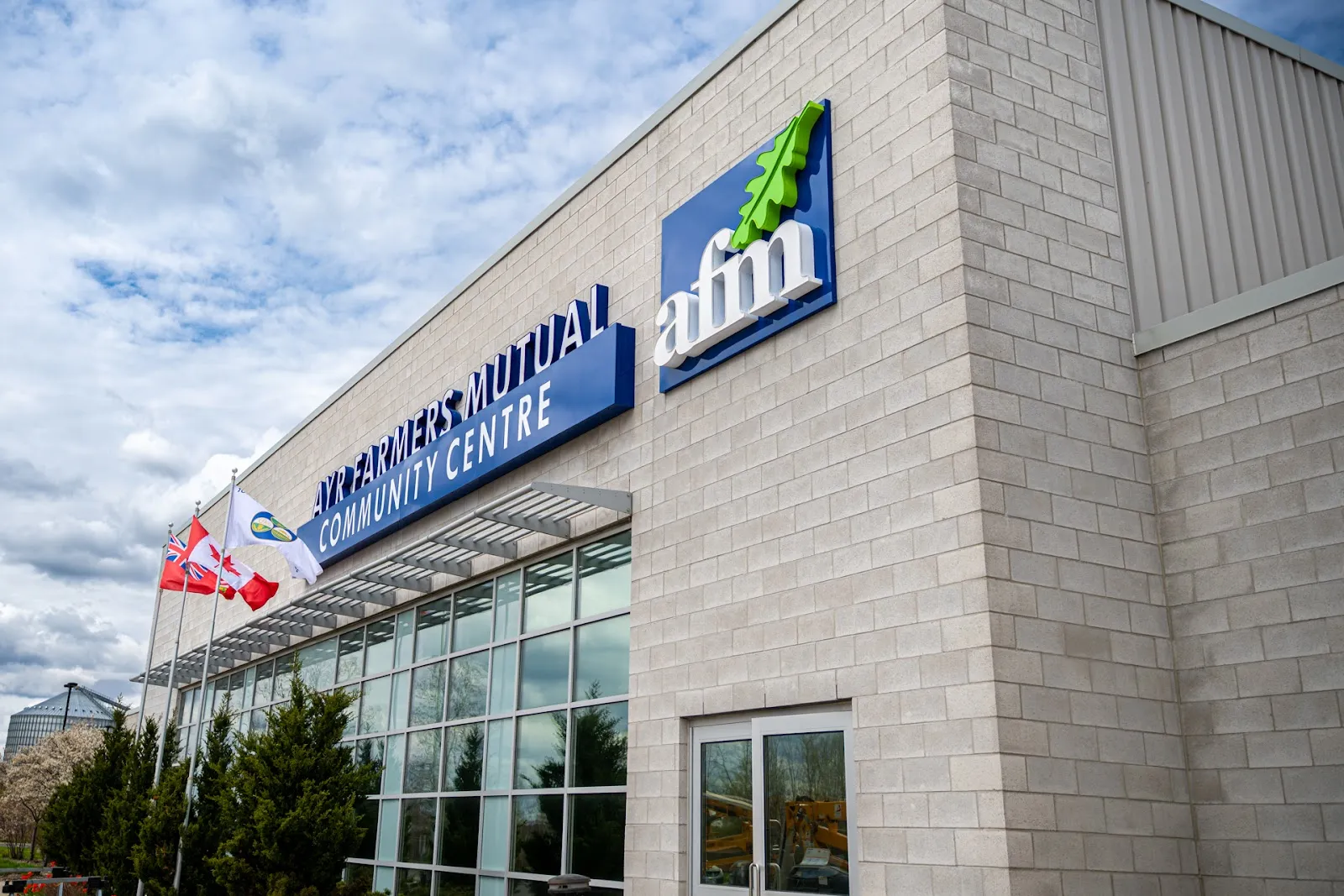 The stone and glass front of the Ayr Farmers Mutual Community Centre with its blue sign — Ayr Farmers Mutual Community Centre