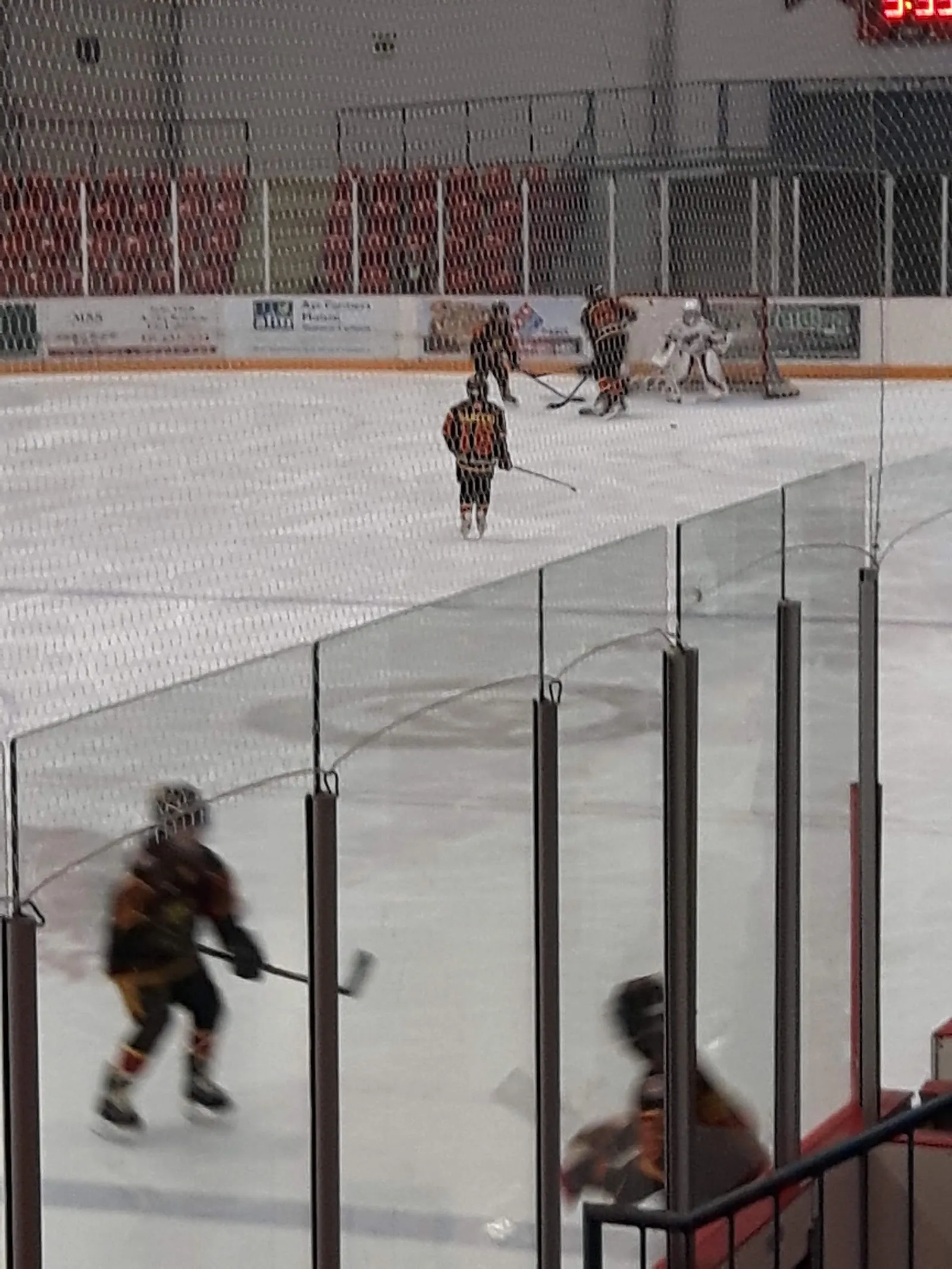 Hockey players on the ice at the Ayr Farmers Mutual Community Centre arena, seen through the glass from the stands — Ayr Farmers Mutual Community Centre