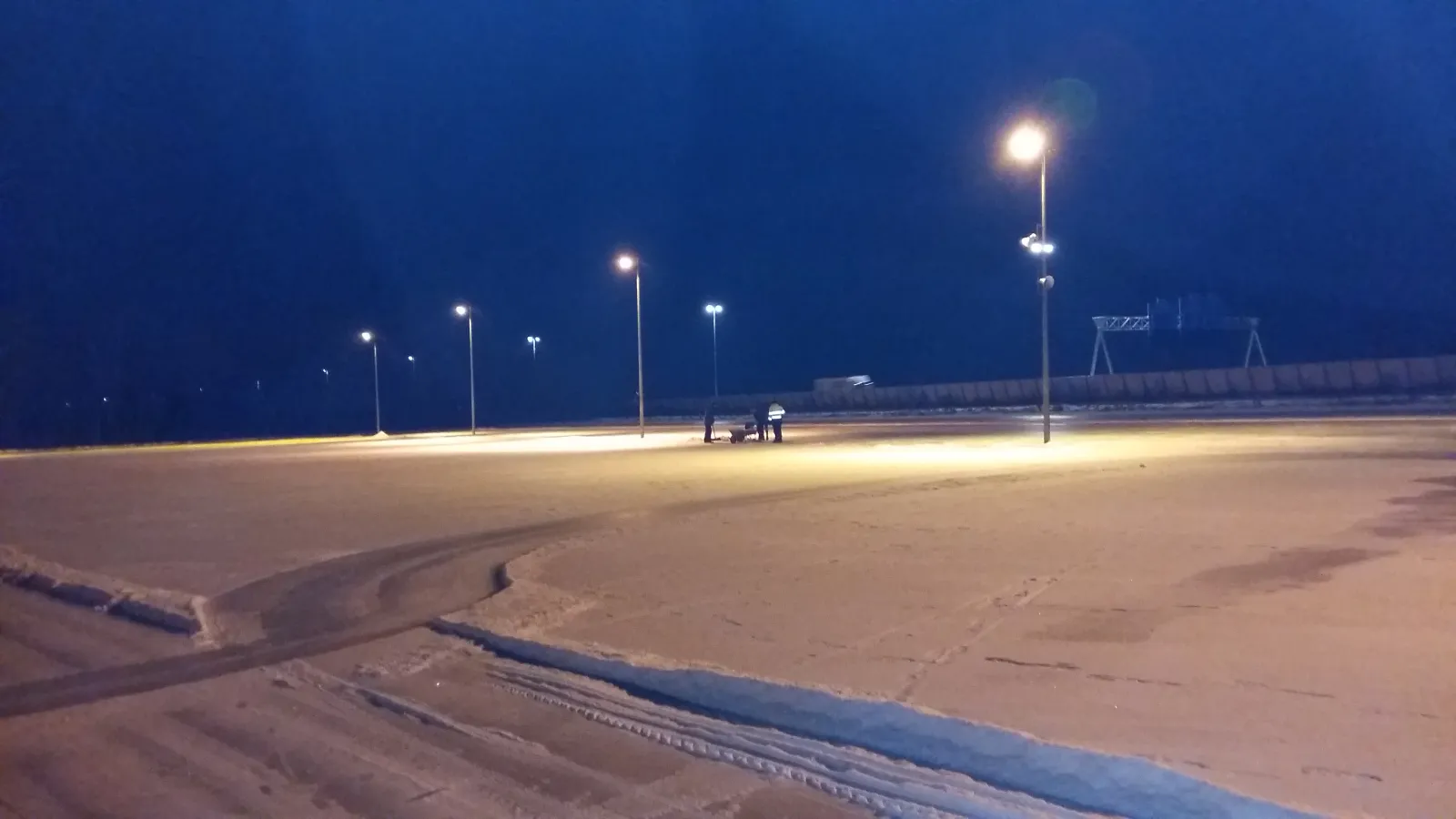 De lege, verlichte ijs- en asfaltvloer van de Baarnse baan in de schemering, met een rij lichtmasten en een spoor van de veger op de voorgrond. – Baarnse IJsbaan