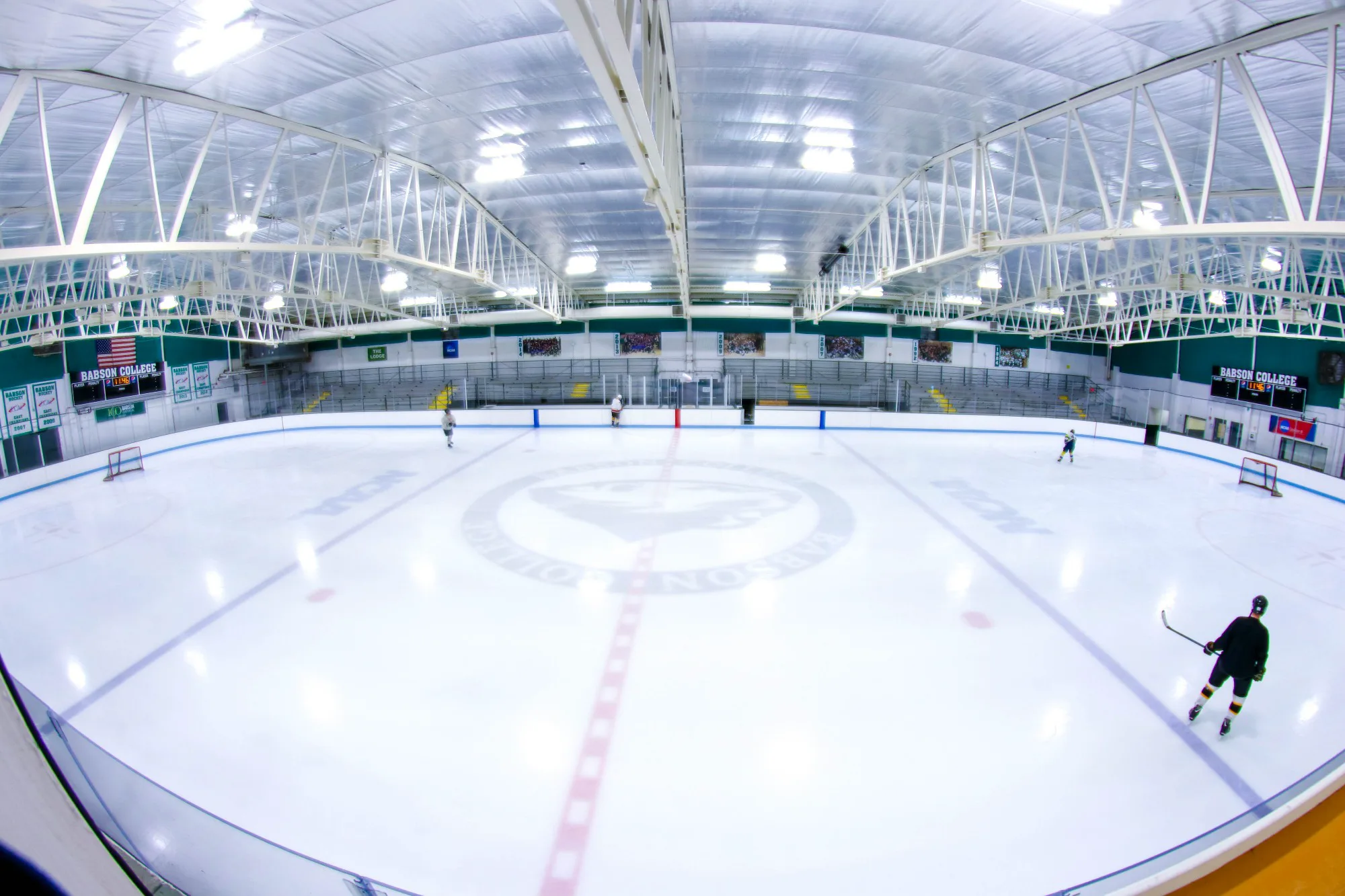 Toda la pista bajo las armaduras blancas del techo en una amplia vista de ojo de pez, con algunos jugadores de hockey en el hielo — Babson Skating Center