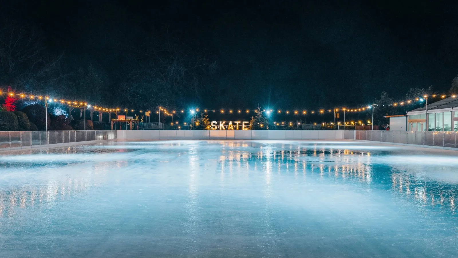 The empty ice of the Bath on Ice rink at night, with the SKATE sign and festoon lights along the far side — Bath on Ice