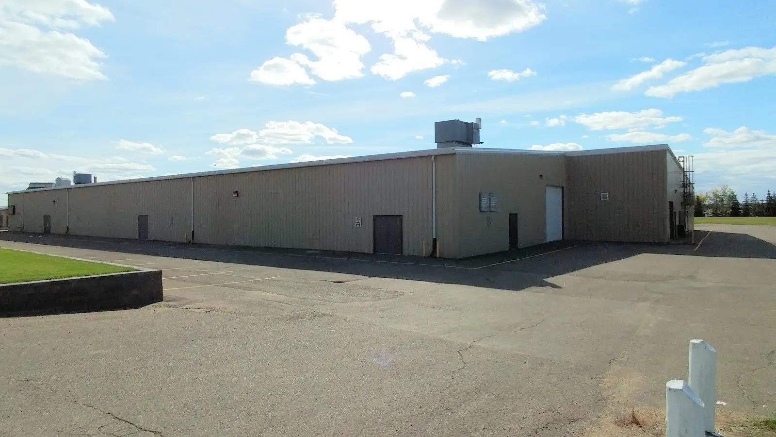 The long beige metal-clad side of the Battleford Arena building, with its parking lot in front. — Battleford Arena