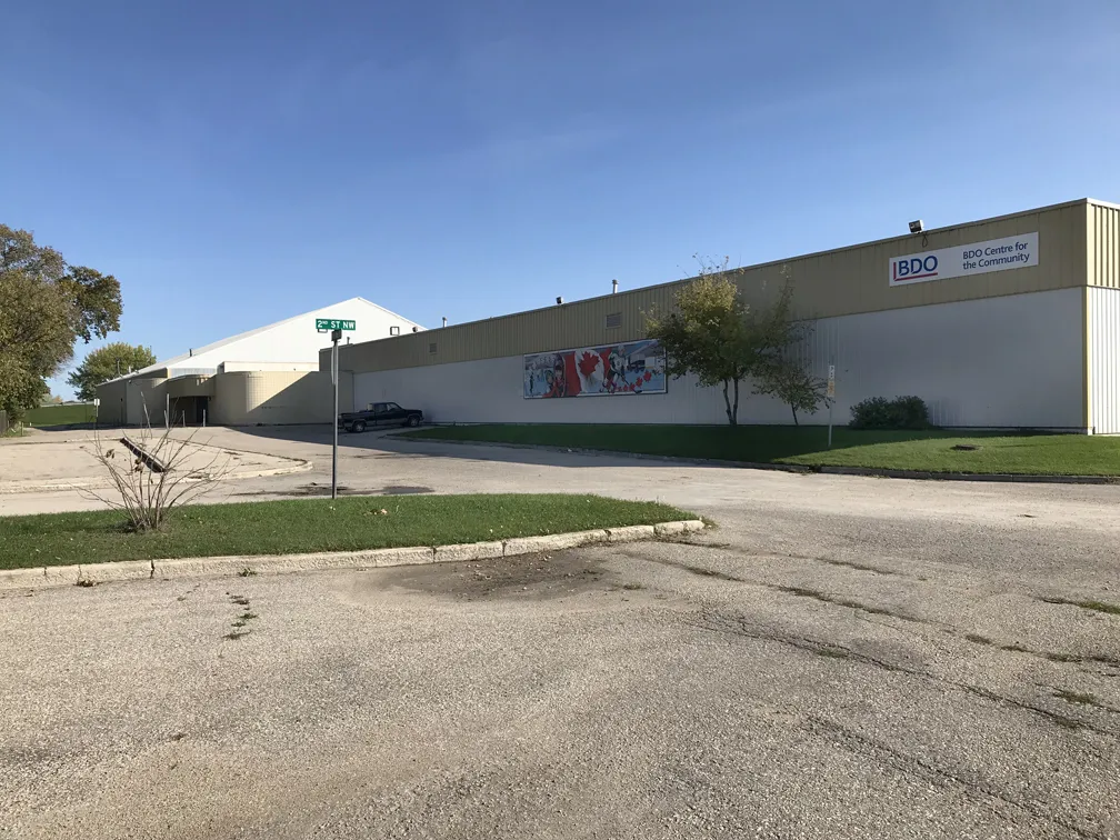 La larga pared beige del BDO Centre con su letrero de BDO y un mural, la arena de techo curvo detrás y un estacionamiento vacío al frente. — BDO Centre for the Community