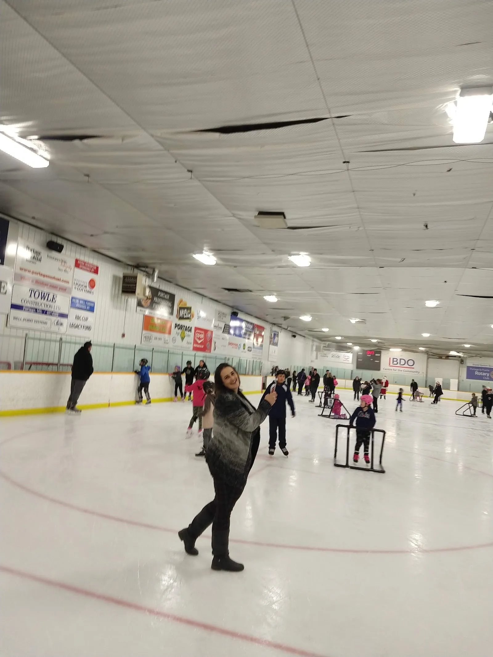 Una sesión pública bajo un techo blanco con paneles colgantes, con patinadores repartidos a lo lejos por la pista y unos cuantos andadores sobre el hielo. — BDO Centre for the Community
