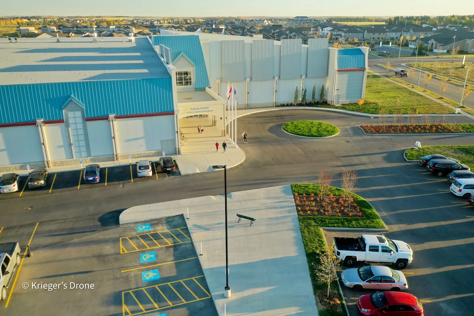 An aerial view of the centre's blue-roofed front entrance, drop-off loop and parking lot. — Beaumont Sport & Recreation Centre