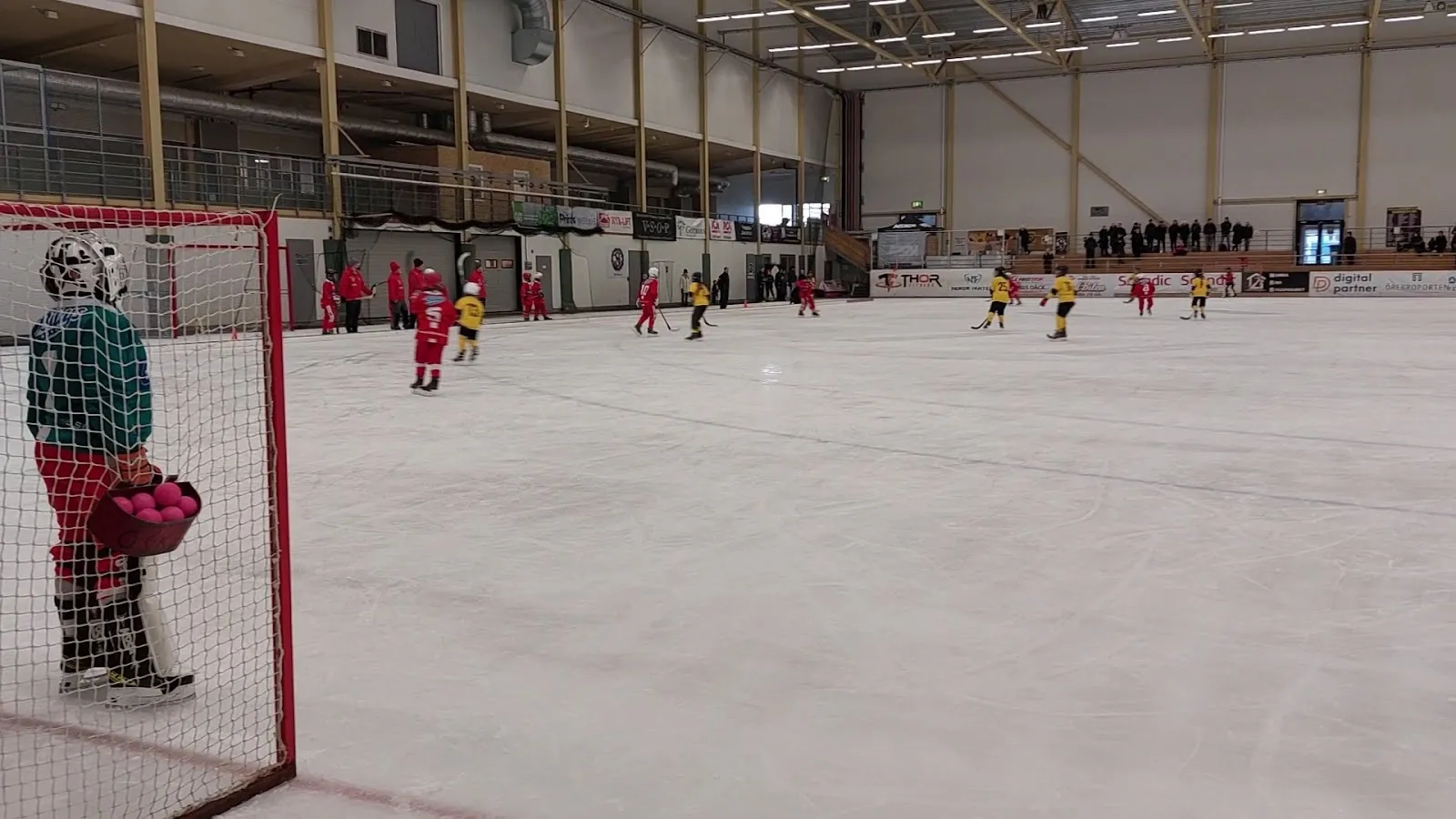 The ice at the Örebro winter stadium with a player beside a goal and the hall wall with its advertising behind. — Behrn Arena bandyhallen