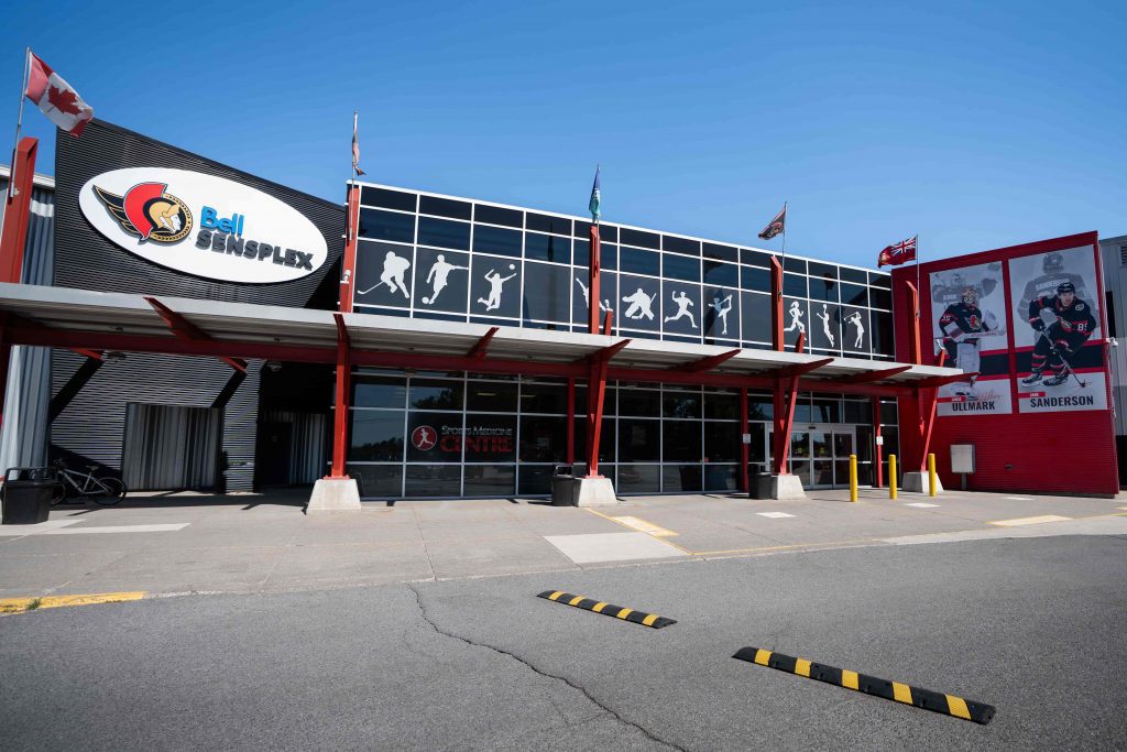 La entrada de Bell Sensplex en Maple Grove Road, con su marquesina roja y gráficos de hockey. — Bell Sensplex