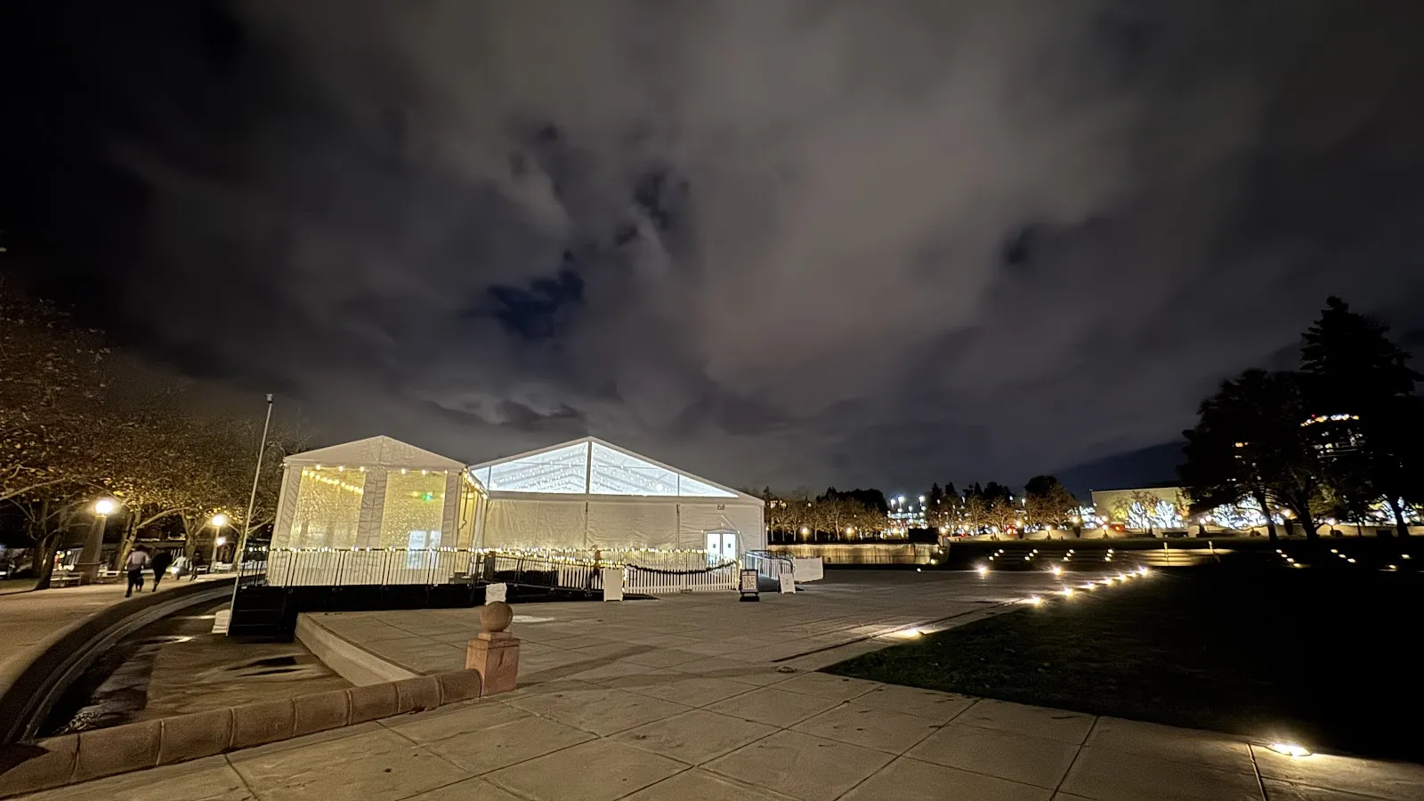 The rink's two white tents lit on a paved plaza in Bellevue Downtown Park at night, seen from a walkway across the lawn. — Bellevue Downtown Ice Rink
