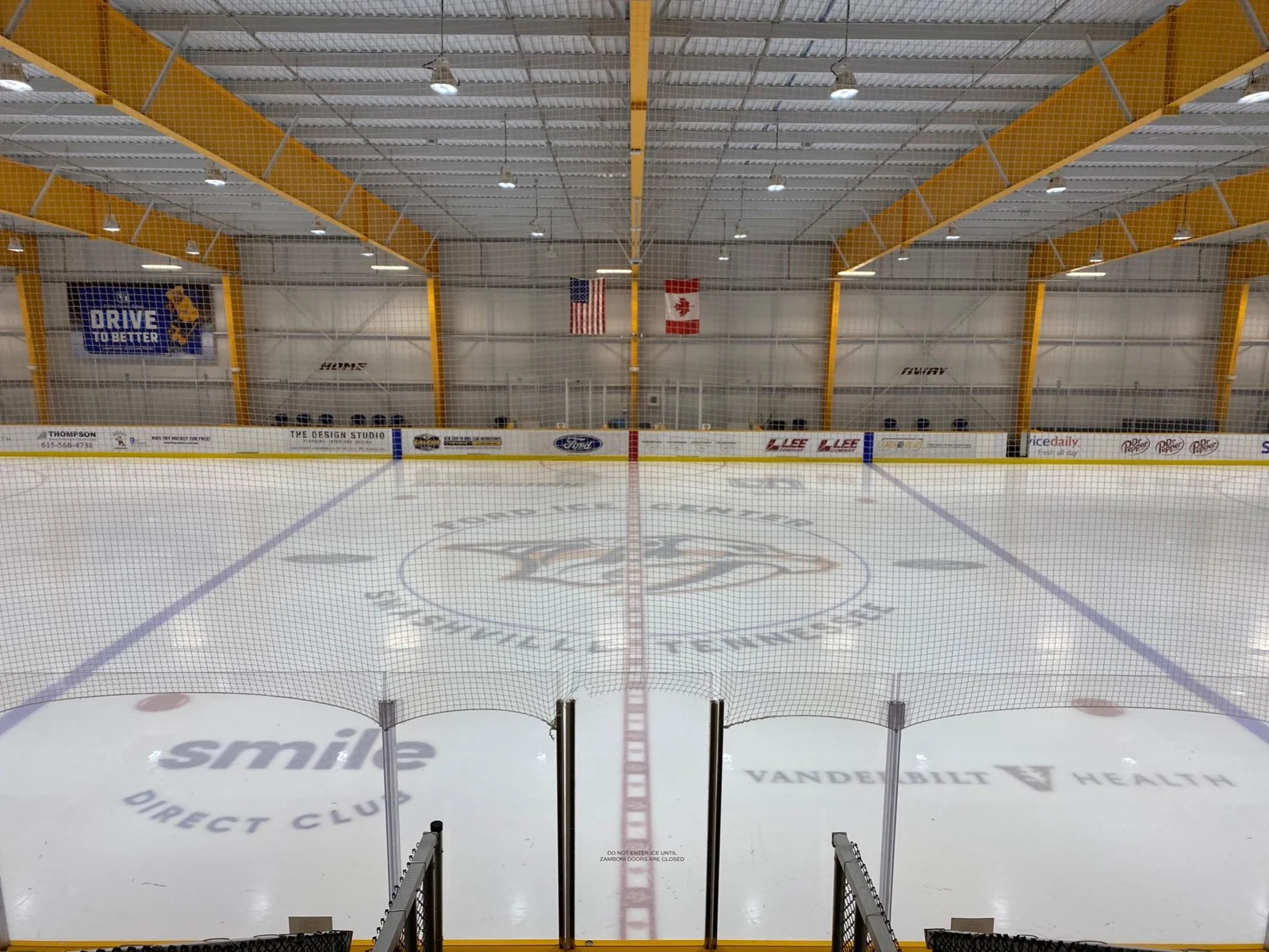 The full ice sheet viewed from the center line beneath yellow roof beams — Ford Ice Center – Bellevue