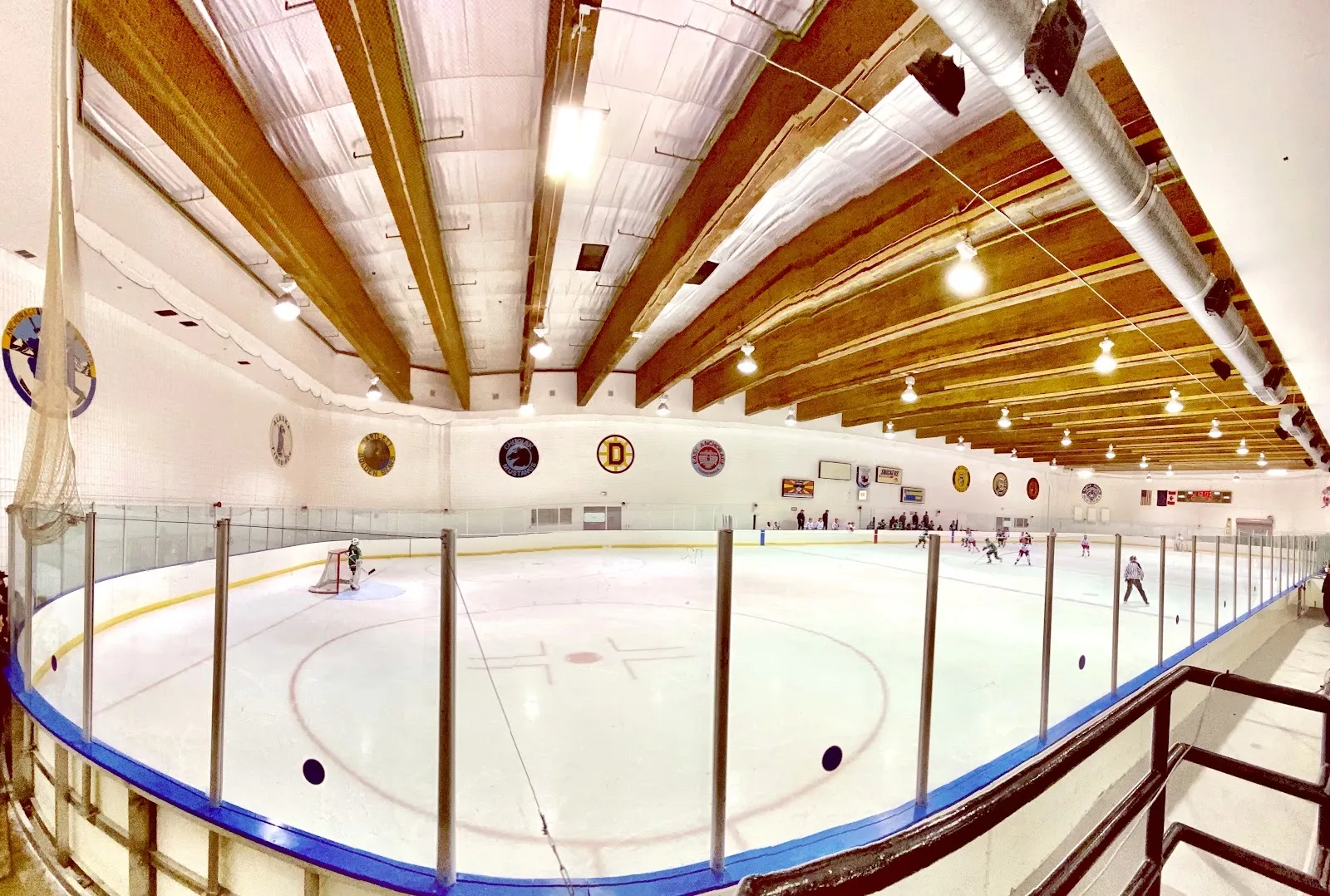 A Ben Boeke sheet in a wide panorama from the stands, under wooden roof beams with Anchorage high school crests along the wall — Ben Boeke Ice Arena