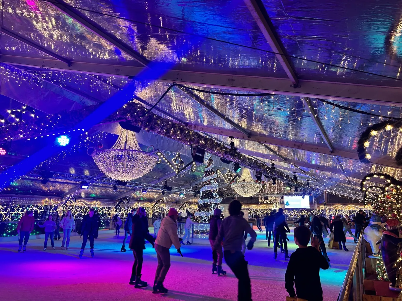 A crowd of skaters seen from behind on the lit ice of the covered Bergs Winterparadijs rink, under a tent roof hung with chandeliers and garlands — Bergs Winterparadijs