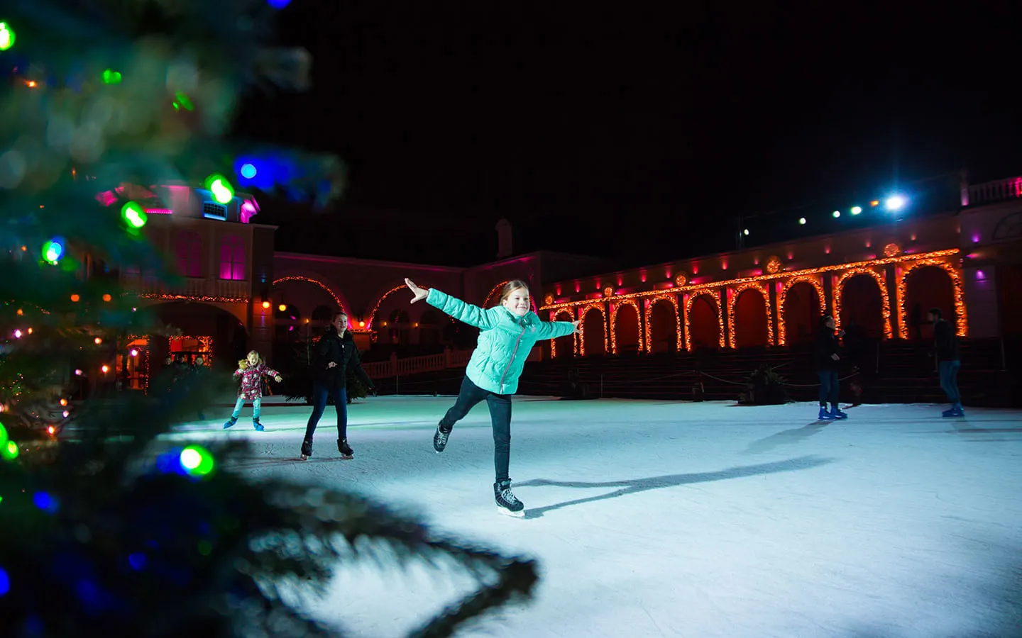 Ein Eisläufer auf der Bahn des Berliner Eislaufens beim Wintertraum im Phantasialand, mit den Lichtern des Themenbereichs Berlin dahinter – Berliner Eislaufen at Phantasialand Wintertraum