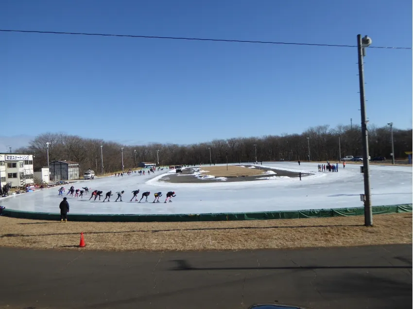 Skaters line up at the start of a race on the frozen 400 metre oval of the Betsukai town rink, with the management building and floodlights beside the track. — Betsukai Town Skate Rink