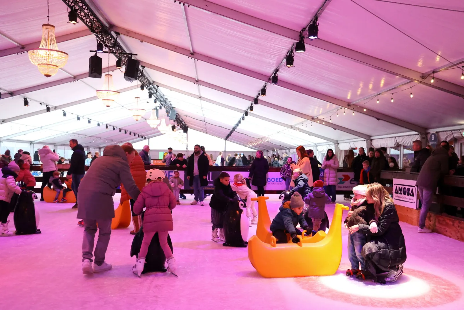Public skating on the pink-lit ice inside the Beuningen on Ice tent, with the penguin skating aids and families on the rink – Beuningen On Ice (Beuningen Gld)