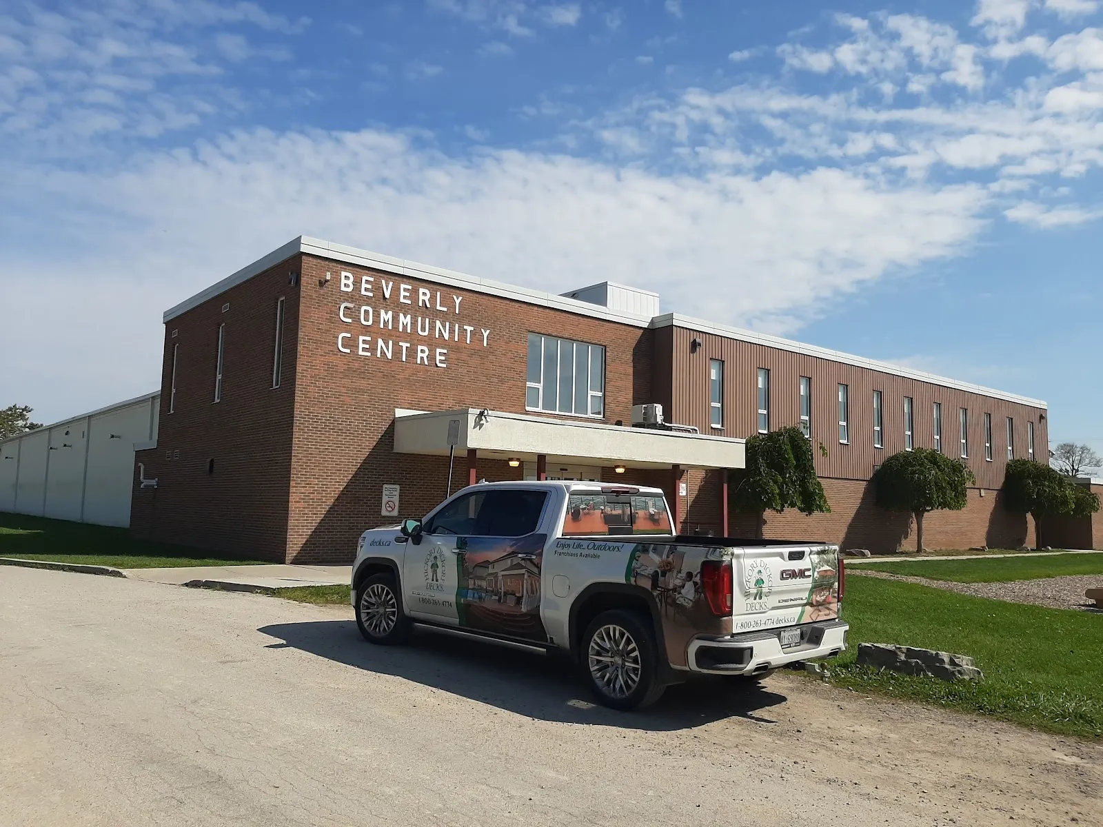 El frente de ladrillo del Beverly Community Centre con su nombre en letras, con una camioneta estacionada sobre la grava al frente bajo un cielo azul. — Beverly Arena