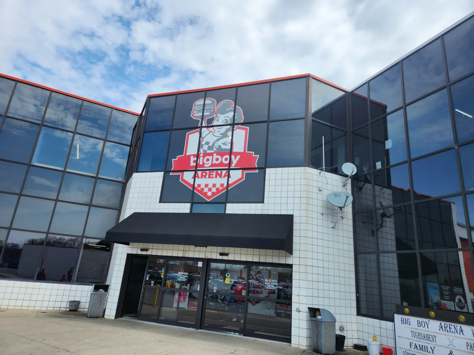 Entrada principal de Big Boy Arena: fachada de muro cortina de vidrio con el letrero rojo y blanco del logotipo "bigboy ARENA", un toldo negro sobre las puertas principales y la marquesina de "BIG BOY ARENA" a nivel de la calle. — Big Boy Arena