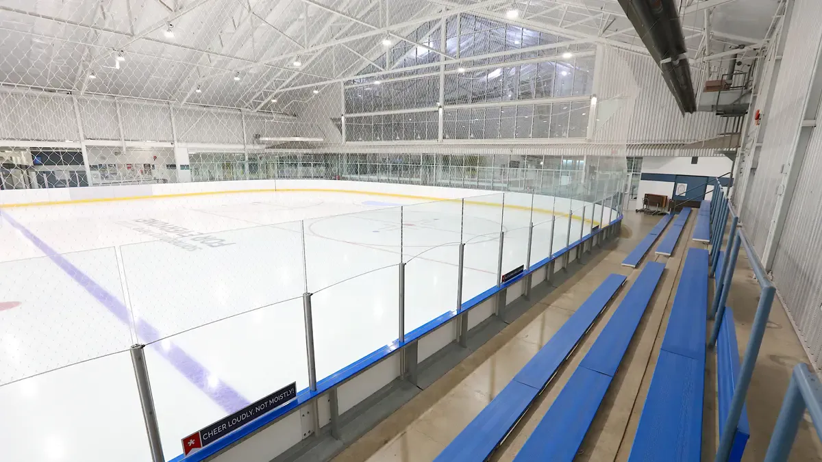 La Cenovus Arena vacía, de tamaño olímpico, desde las gradas azules, bajo un techo blanco con ventanas de claristorio. — Big Marble Go Centre