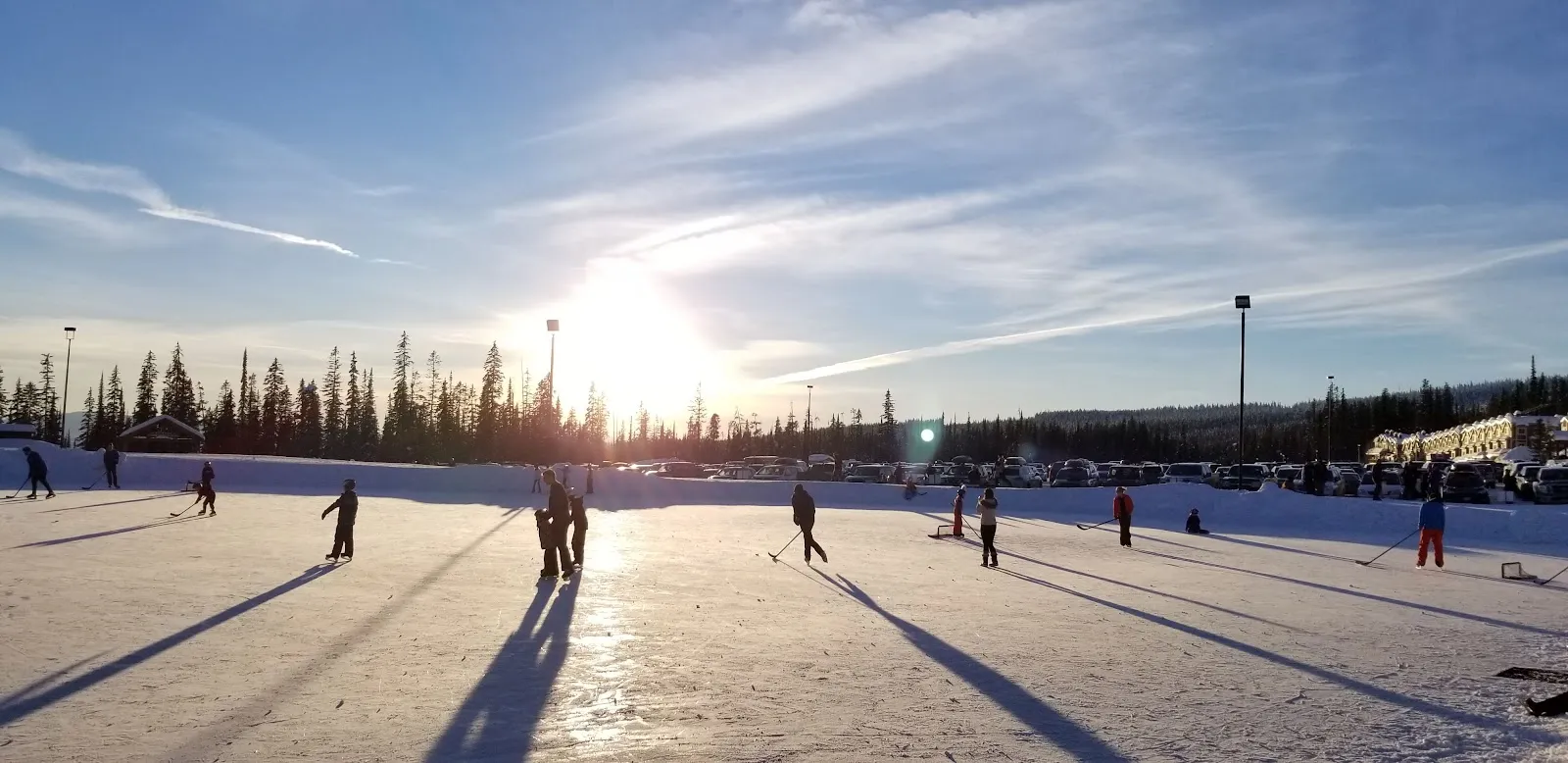 Skaters across the Big White rink at sunset with long shadows on the ice and spruce behind. — Big White Ice Skating Rink
