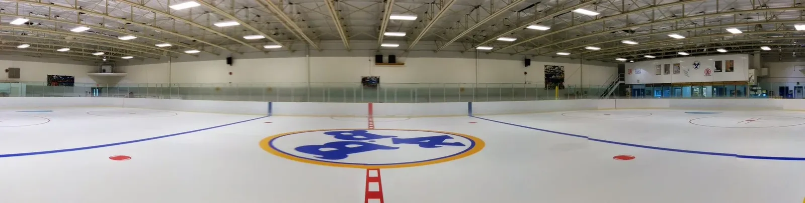 A panorama of the empty ice sheet at Bill Bolton Arena, with the centre-ice logo and the banners along the far wall. — Bill Bolton Arena
