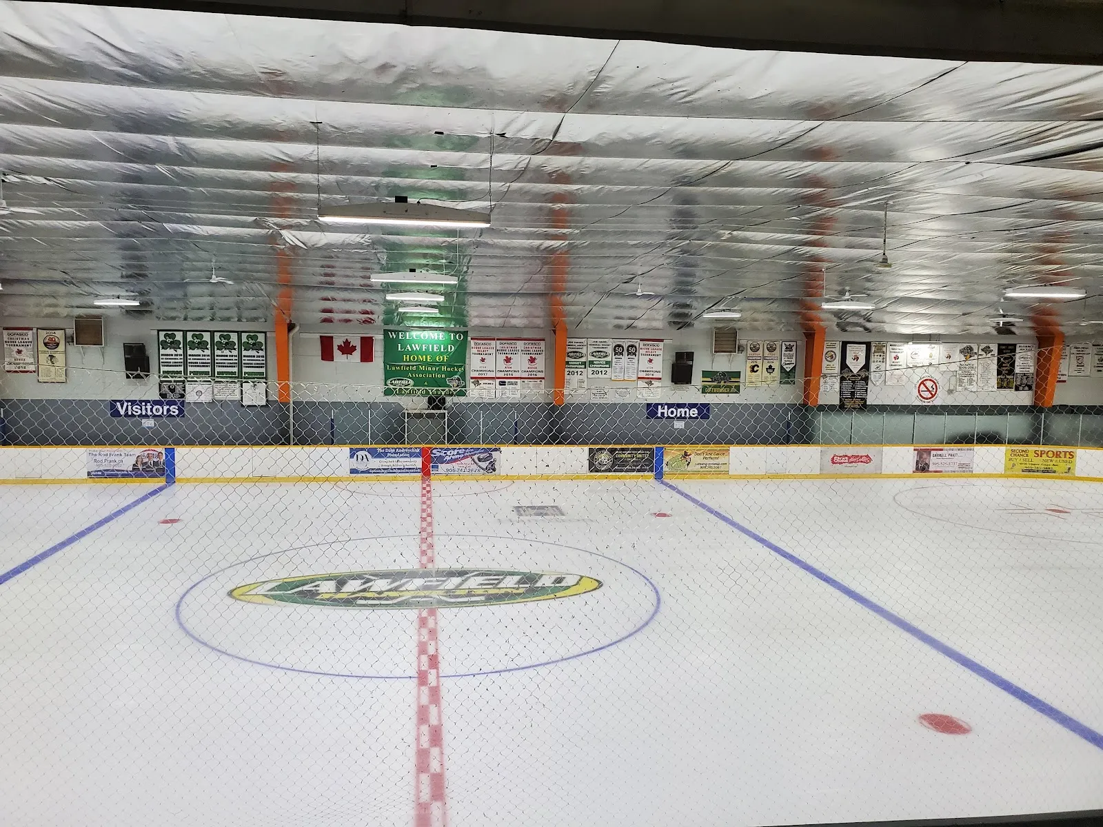 La pista vacía desde un extremo, con un logotipo pintado en el centro de la pista, líneas azules y roja y un techo aislado plateado. — Bill Friday Lawfield Arena
