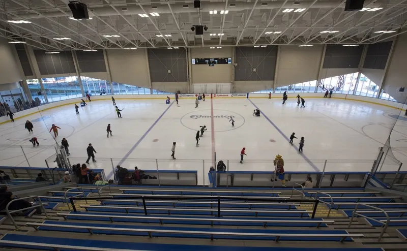A public session on a wide sheet seen from the stands, skaters spread across the ice below a high curved roof with a blue-lined grandstand in front. — Bill Hunter Arena
