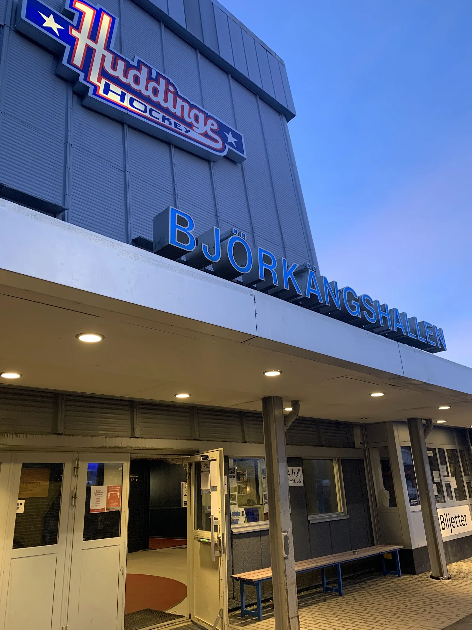 The Björkängshallen entrance with its blue name letters and the Huddinge Hockey sign on the grey wall above the ticket doors — Björkängshallen B-hall
