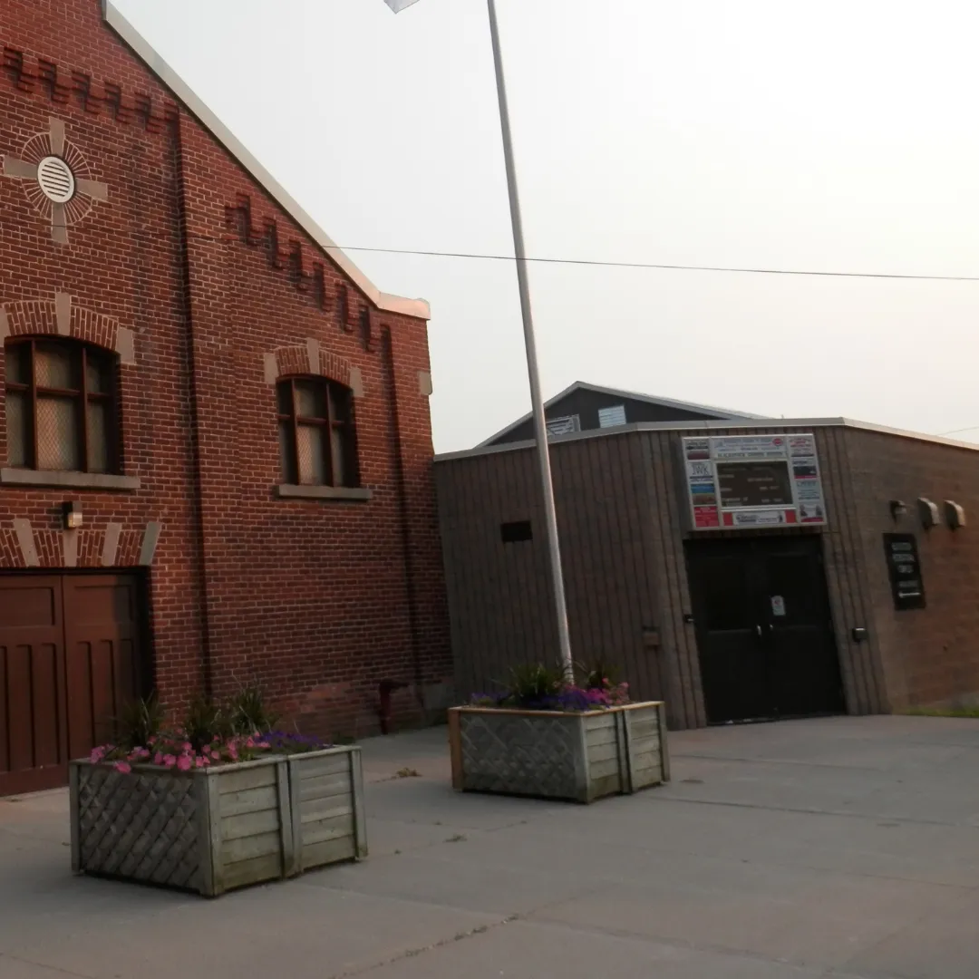 The arena entrance beside the red-brick hall, with planters and a flagpole out front. — Blackstock Arena