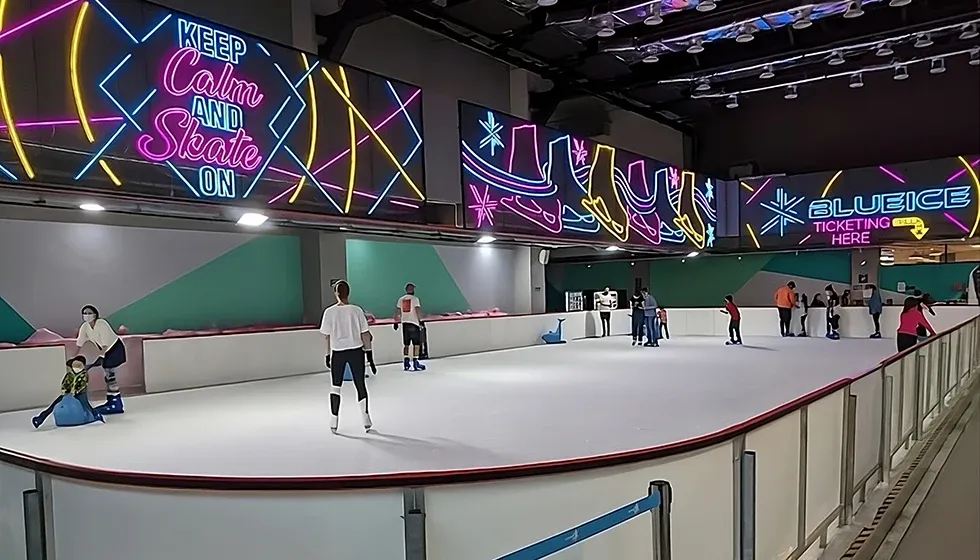 The compact sheet at Sunway 163 Mall seen from the barrier, with a neon Blue Ice sign over the far dasher and skaters on the ice. — Blue Ice Skating Rink Sunway 163 Mall