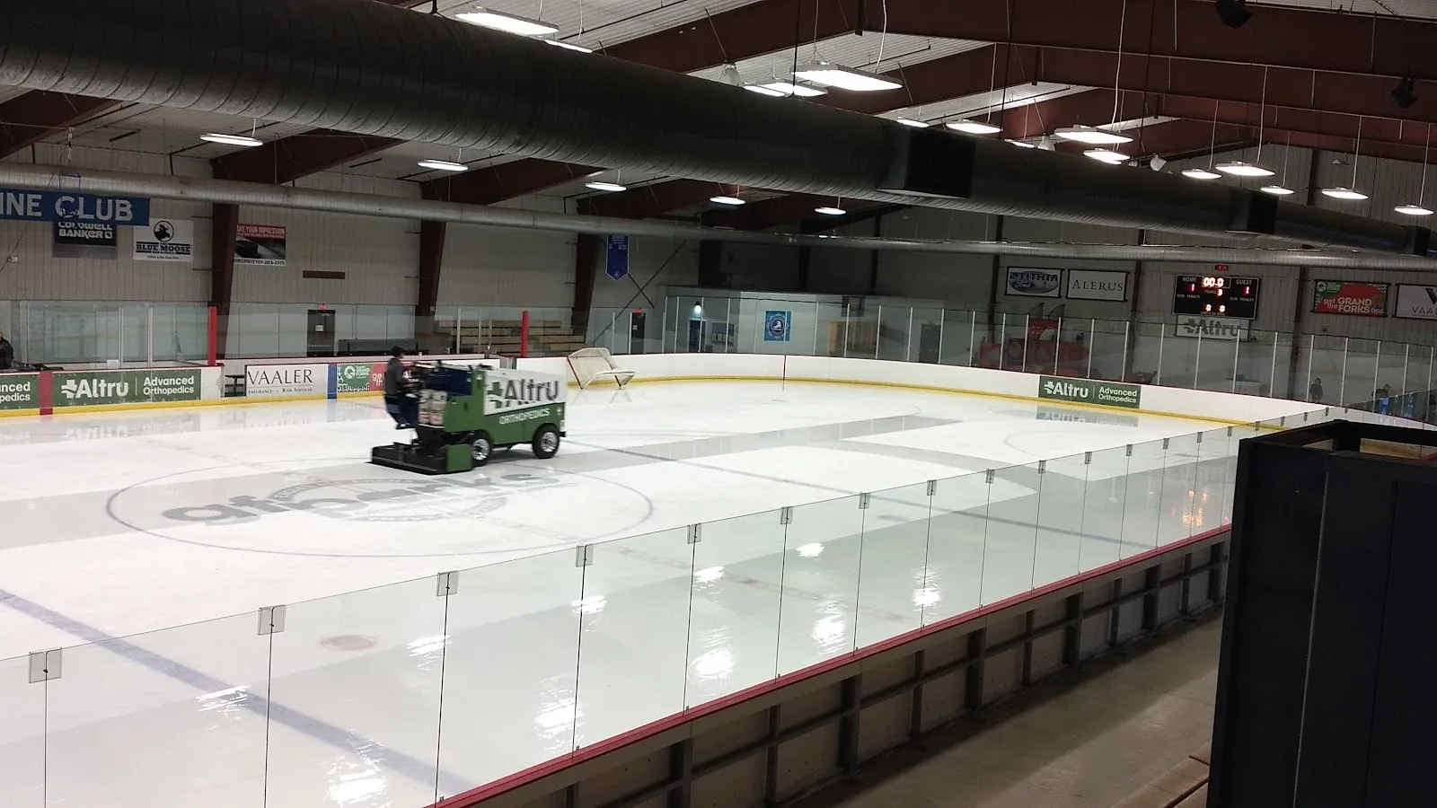 La máquina alisadora sobre el hielo recién inundado en Blue Line Club IcePlex, vista por encima del vidrio desde las gradas, con anuncios de Altru en el lado opuesto. — Blue Line Club IcePlex