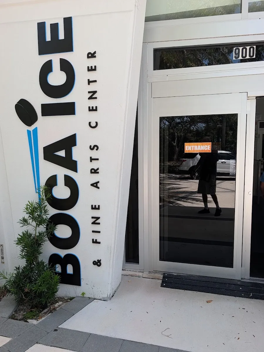 Main entrance of the building: a white angled wall panel with large black "BOCA ICE & Fine Arts Center" lettering and a puck-and-stick logo beside a glass door marked ENTRANCE, with the street number 900 above the door. — Boca Ice (Boca Raton)