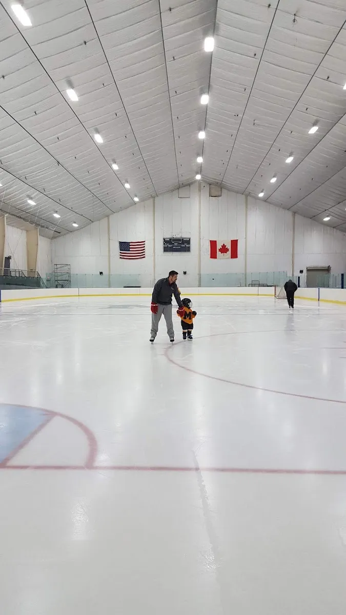 A wide view down the Bontecou Rink with a coach crossing the ice, school flags on the end wall and a few players far away. — Bontecou Rink at Millbrook School