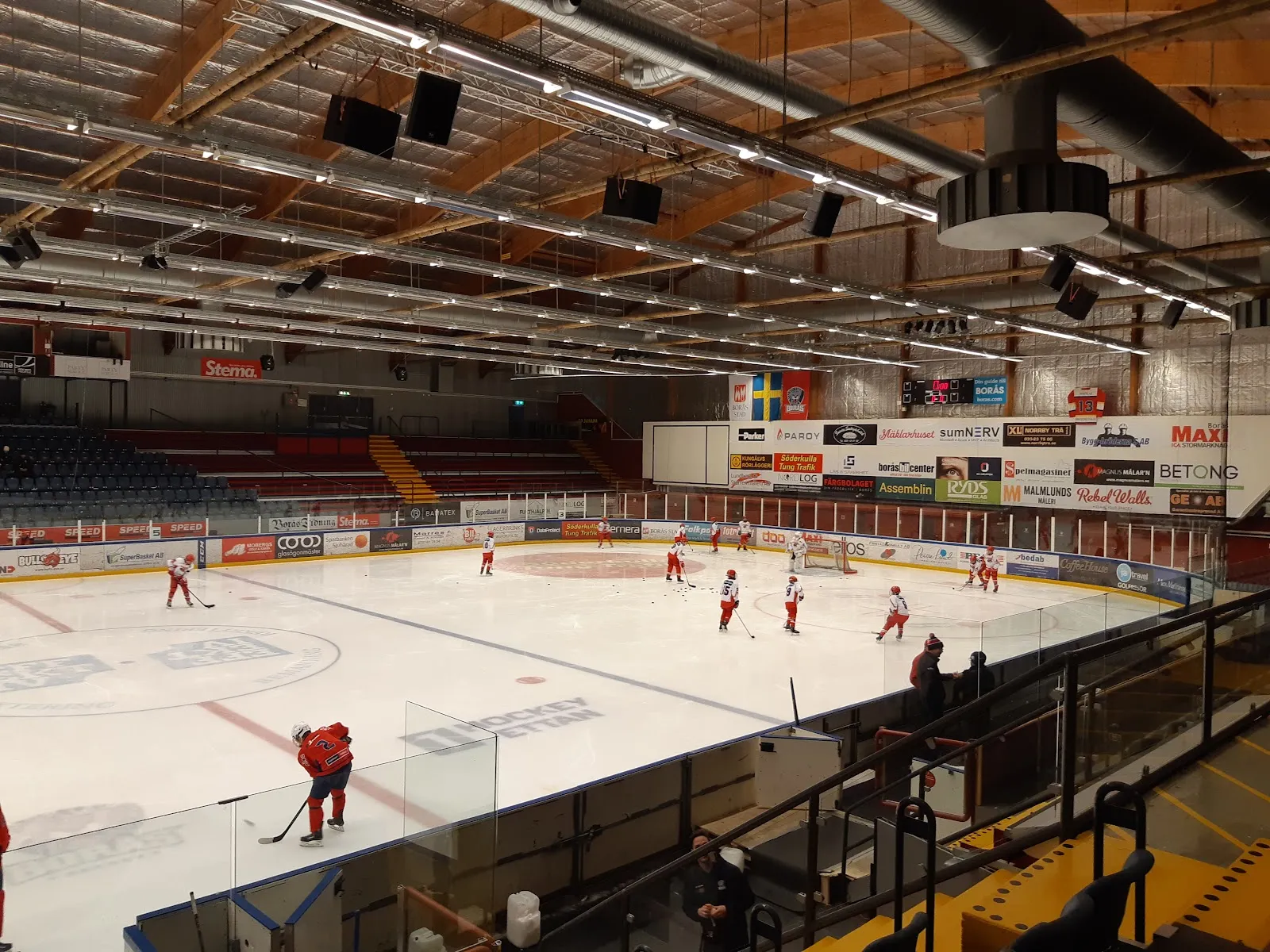Isen och läktarna i Borås Ishall sedda från de övre raderna, med några åkare på isen – Borås Ishall