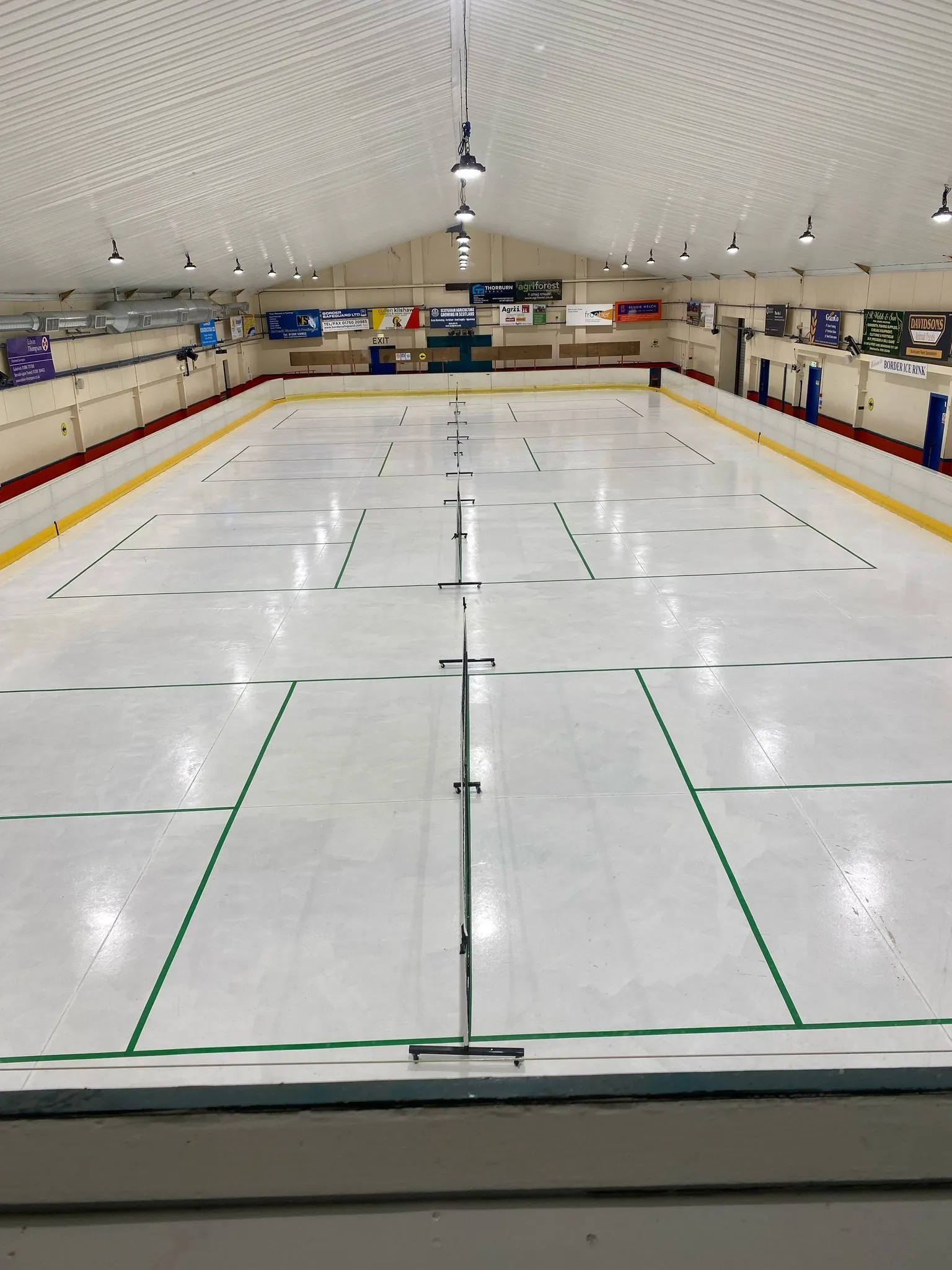 The empty ice sheet at Border Ice Rink under the long pitched roof, with the boards and curling lines marked — Border Ice Rink