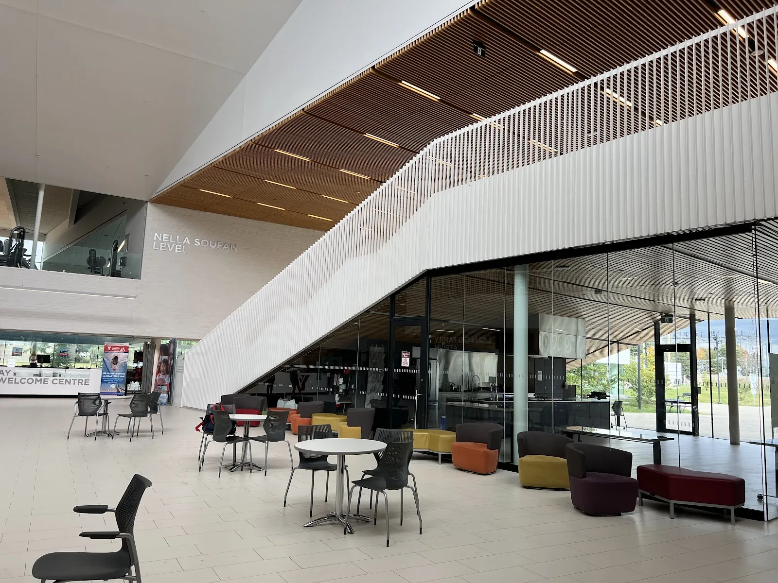 El vestíbulo del StarTech.com Community Centre: un atrio alto con una escalera de barandales blancos, mesas de café y sillones, y el centro de bienvenida al fondo. — Bostwick Arena