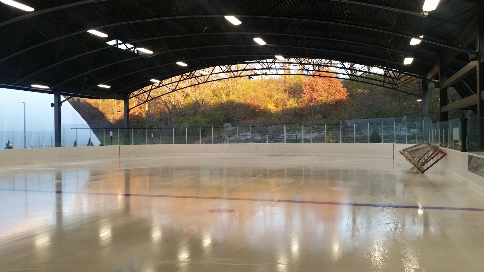 Una pista techada de Braemar Arena bajo un techo de acero en arco, con hielo recién pulido que refleja la ladera otoñal más allá de las vallas — Braemar Arena