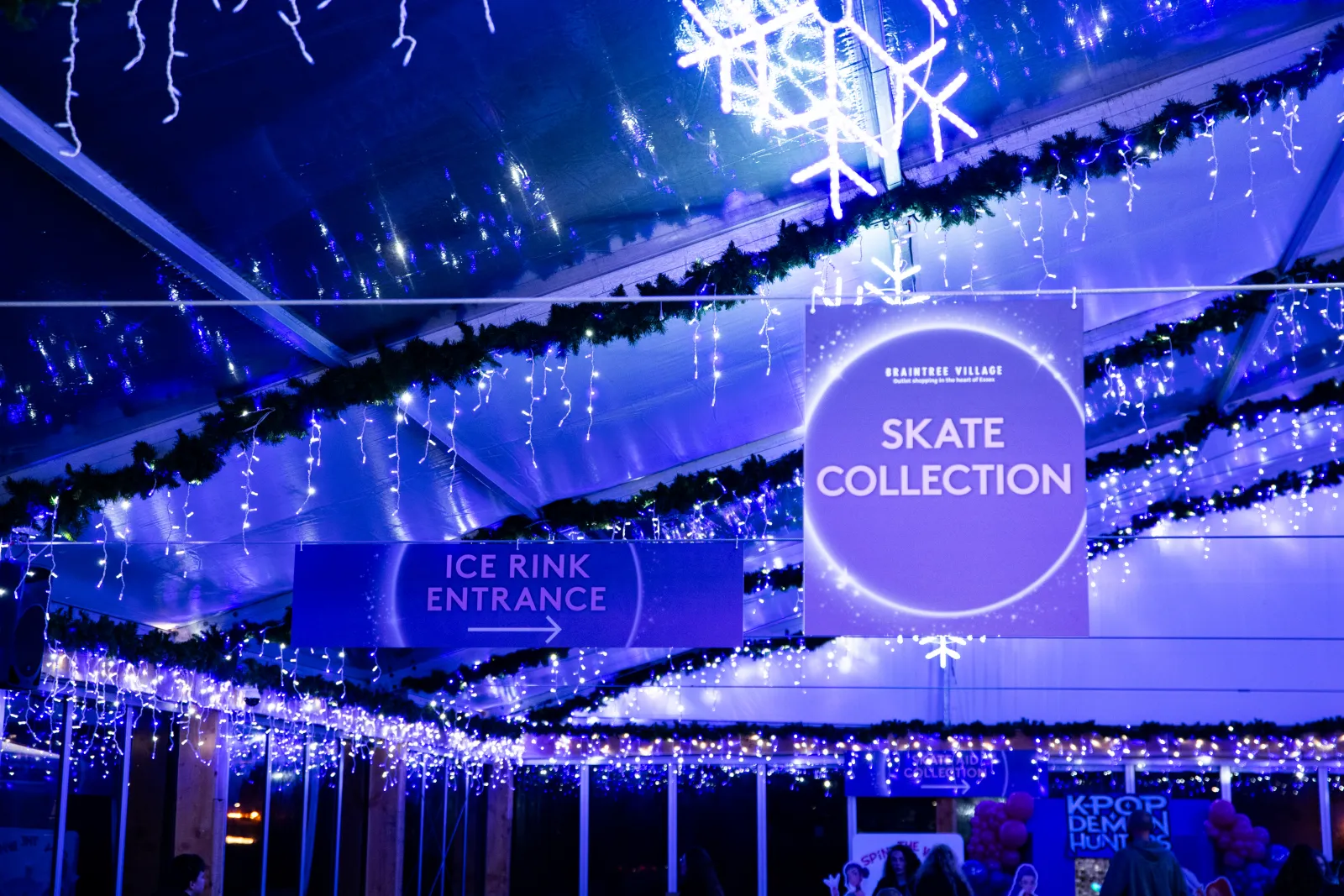 The covered Braintree Village rink entrance, with the Ice Rink Entrance and Skate Collection signs hanging in the festive lights. — Braintree Village Ice Rink