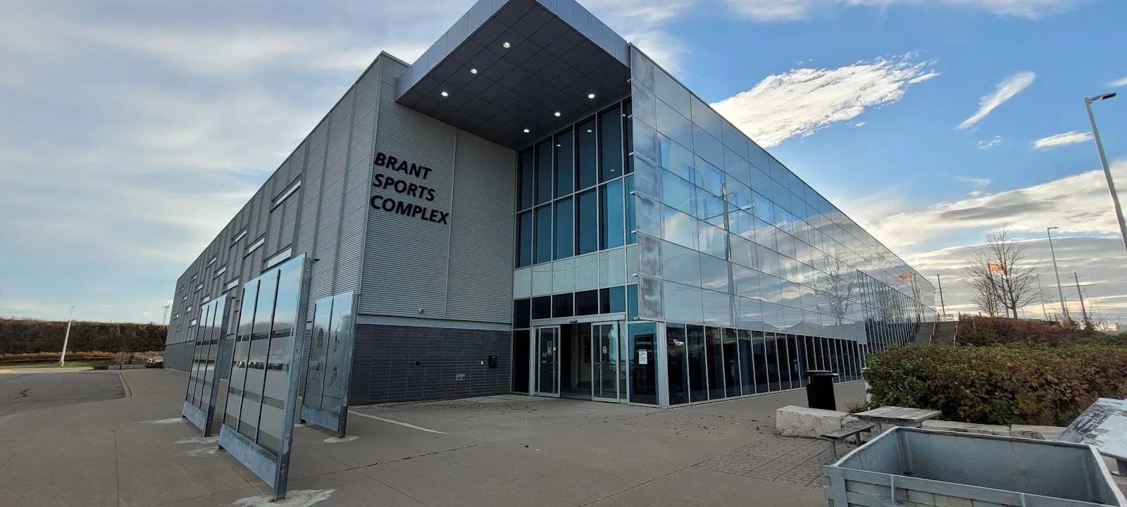 The glass-and-grey-panel front of the Brant Sports Complex under a partly cloudy sky, with the Brant Sports Complex lettering on the corner. — Brant Sports Complex