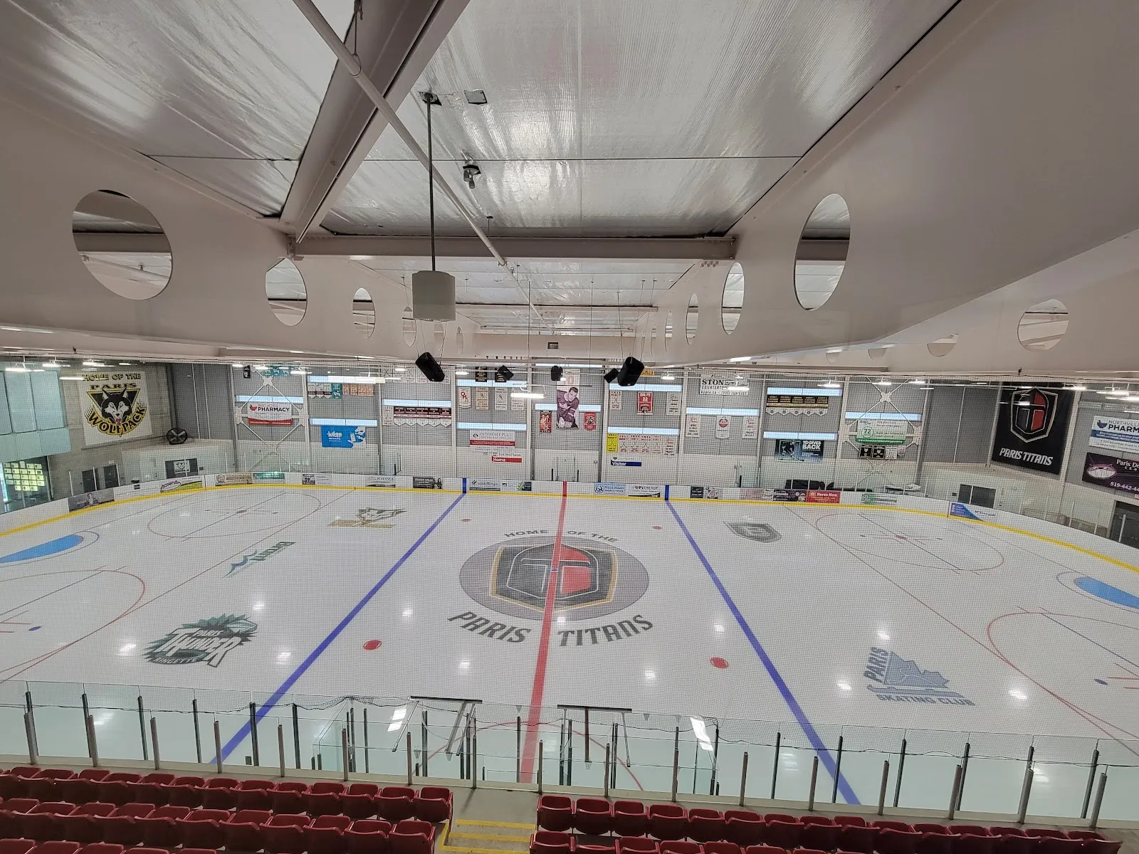 The empty ice sheet at the Brant Sports Complex with the Paris Titans logo at centre ice, the red-seat stands along the glass and banners along the far wall. — Brant Sports Complex