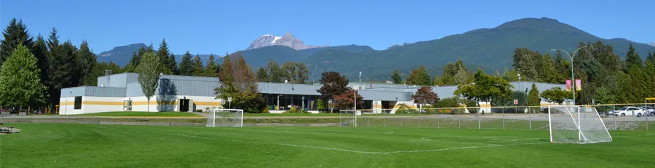 Brennan Park Recreation Centre, 1009 Centennial Way, Squamish: el edificio visto a través del campo deportivo (banner de la página del Distrito de Squamish) — Brennan Park Recreation Centre