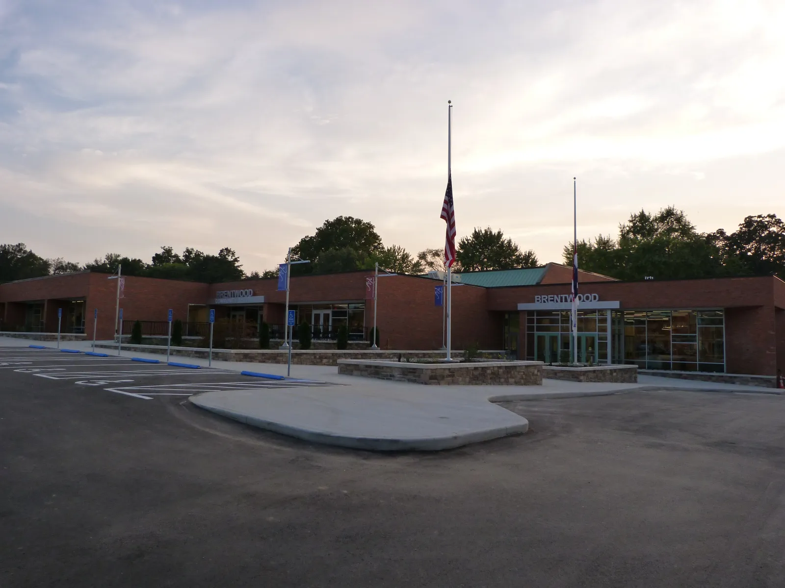 The brick Brentwood Community Center, home of the ice rink, at dawn, with Brentwood signage over the glass doors and a half-mast flag out front. — Brentwood Ice Rink