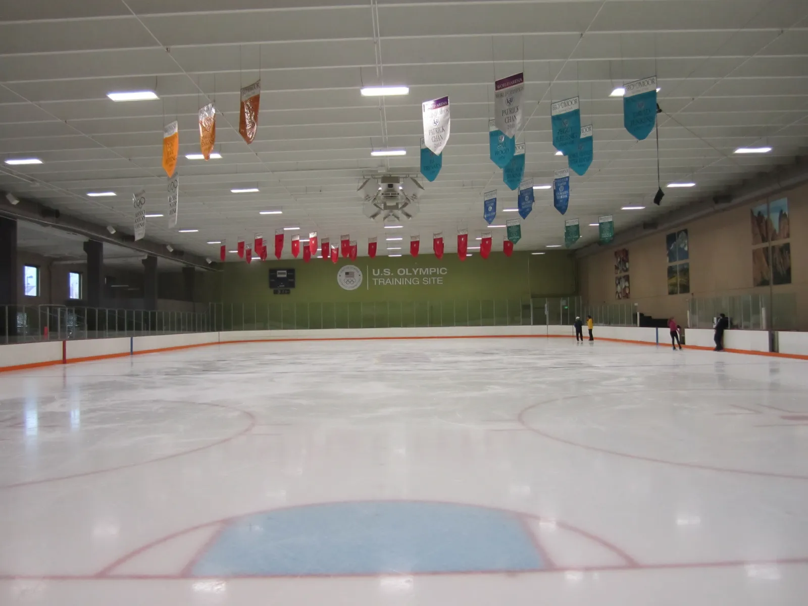 One sheet from the end, with banners hanging from the roof, the U.S. Olympic Training Site sign on the green end wall and a few skaters in the distance. — Broadmoor World Arena Ice Hall