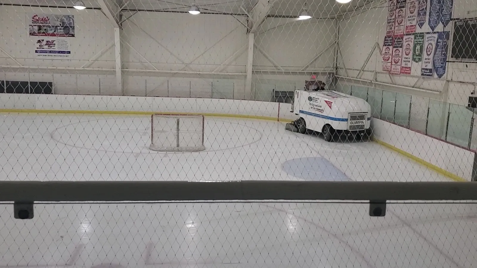 El hielo vacío de Brockville Centennial Youth Arena detrás de la red de seguridad, con la pulidora, una portería y mantas de clubes en el muro del fondo — Brockville Centennial Youth Arena
