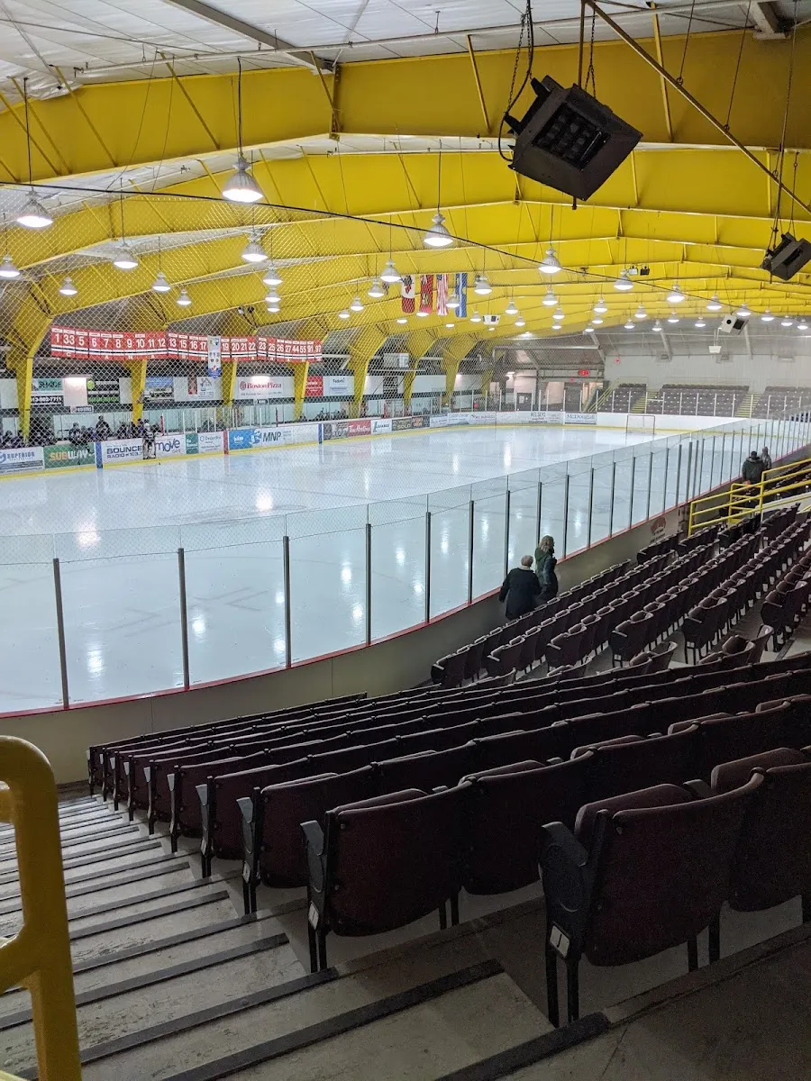 El hielo del Memorial Centre desde las filas superiores de asientos color vino, bajo las armaduras amarillas del techo. — Brockville Memorial Civic Centre