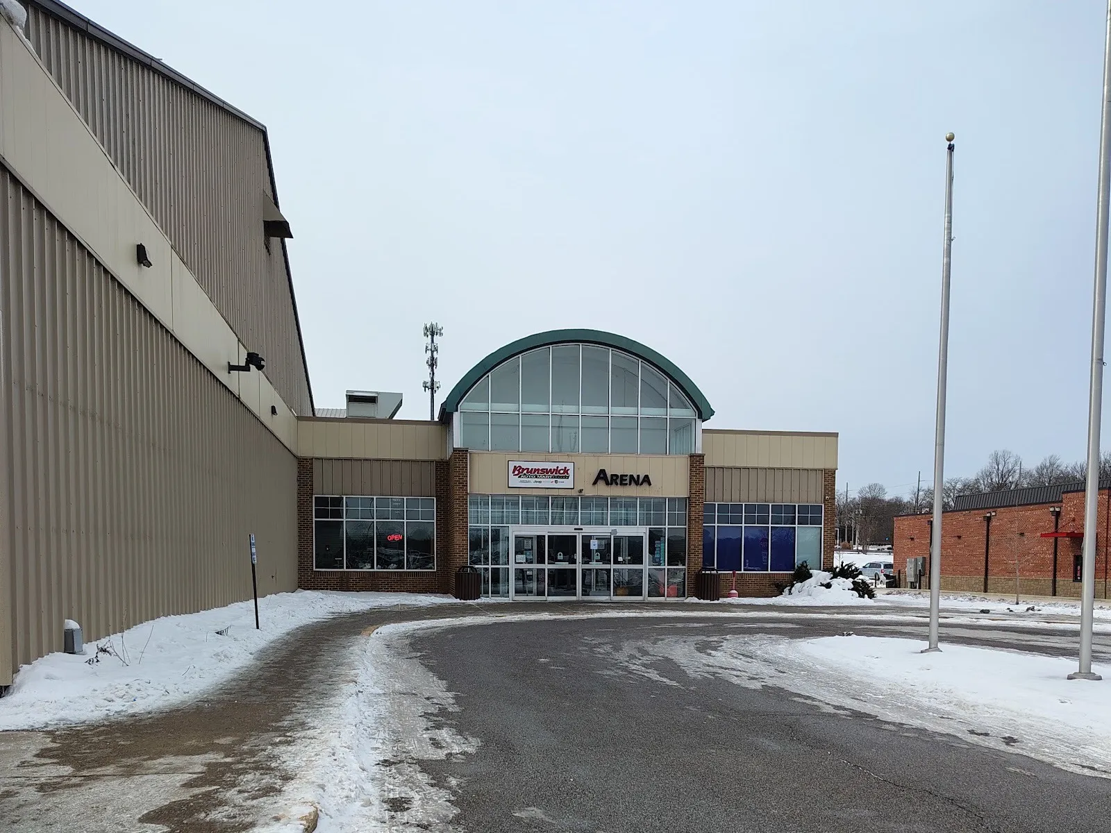 The Brunswick Auto Mart Arena entrance in winter: the arched glass lobby with the Arena sign, beside the long metal wall of the rink hall — Brunswick Auto Mart Arena (Strongsville)