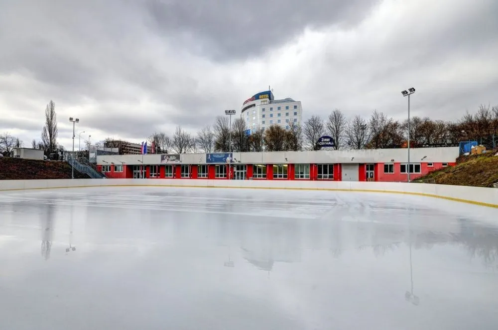 The 40 by 30 metre outdoor ice surface at Bruslení za Lužánkami with the changing-room building behind — Bruslení za Lužánkami